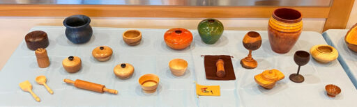 A table full of turned items: bowls, hollow forms, goblets, lidded boxes, a roller pin, and a set of spoon and spatula.