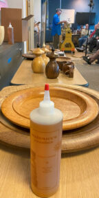 A bottle of Mahoney's Finishes with Mike Mahony demonstrating woodturning in the background